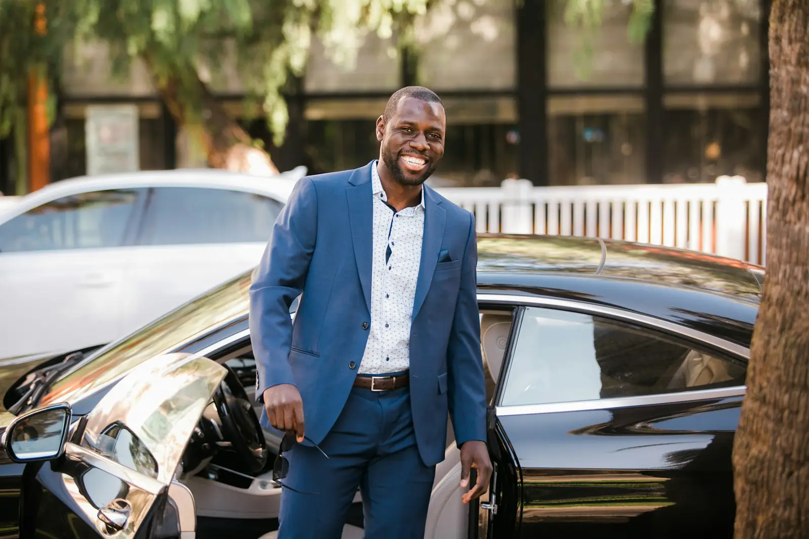 Homme souriant en costume devant une voiture noire